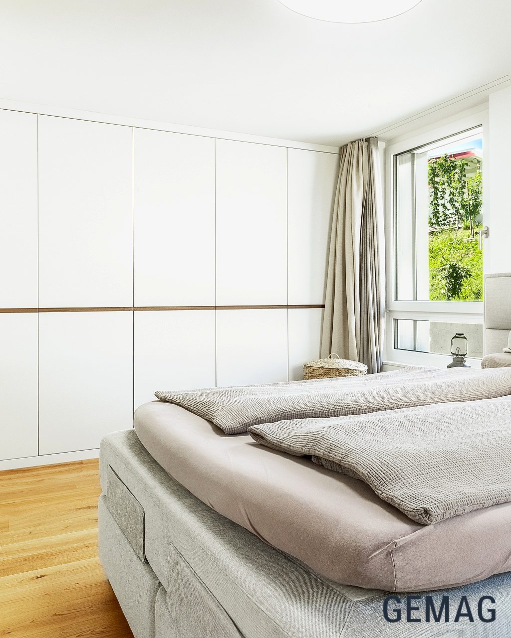 Schlafzimmer mit Doppelbett, weissem Einbauschrank und Fenster mit Grünblick, Parkettboden.