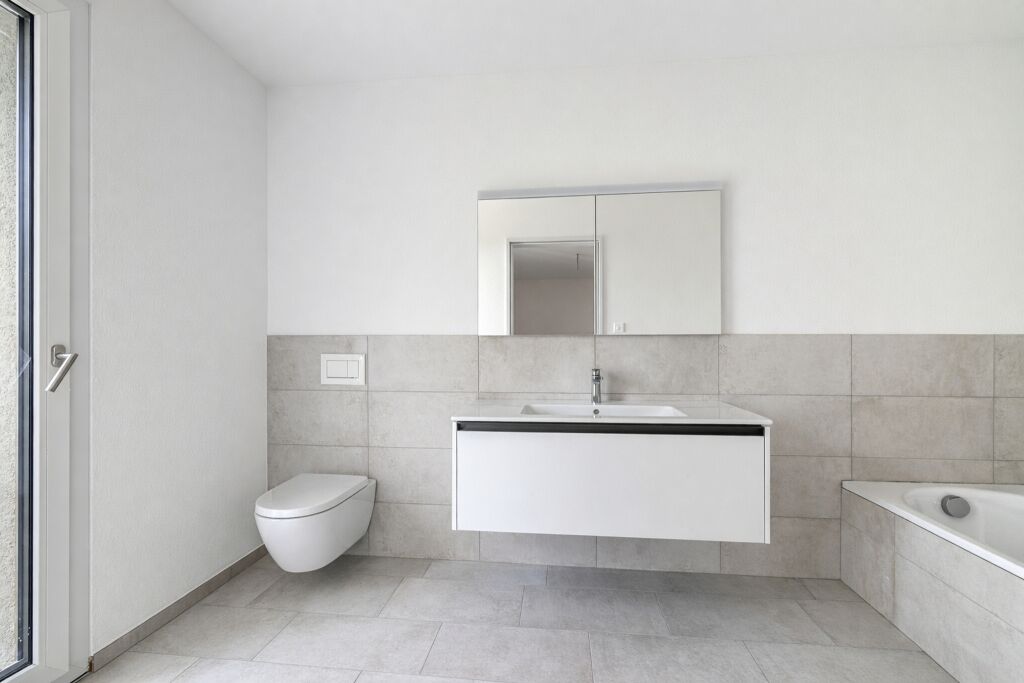 Badezimmer mit schwebendem Waschtisch, Spiegelschrank, Wand-WC und Badewanne, helle Steinfliesen.