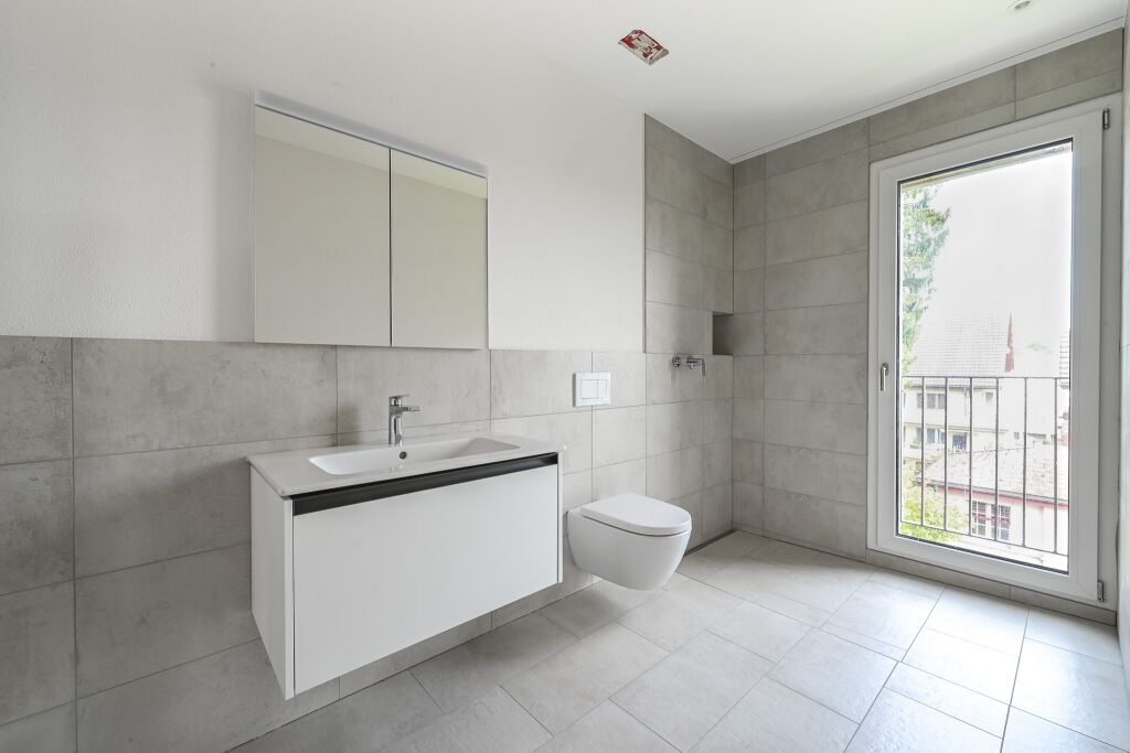Badezimmer mit schwebendem Waschtisch, Spiegelschrank, Wand-WC und grossem Fenster mit Blick ins Freie.
