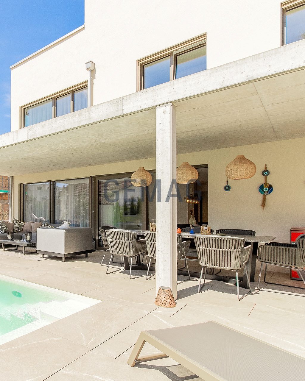 Überdachte Terrasse mit Aussenlounge und Pool, seitlich Blick auf die moderne Hausfassade.