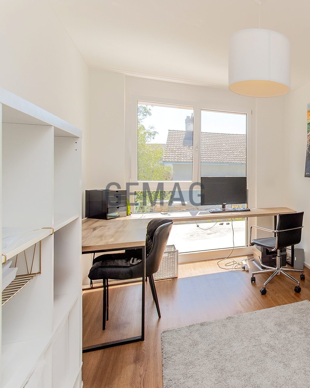Arbeitszimmer mit Schreibtisch am Fenster, Bürostuhl, weissem Sideboard und Holzparkett, Blick Richtung Garten.