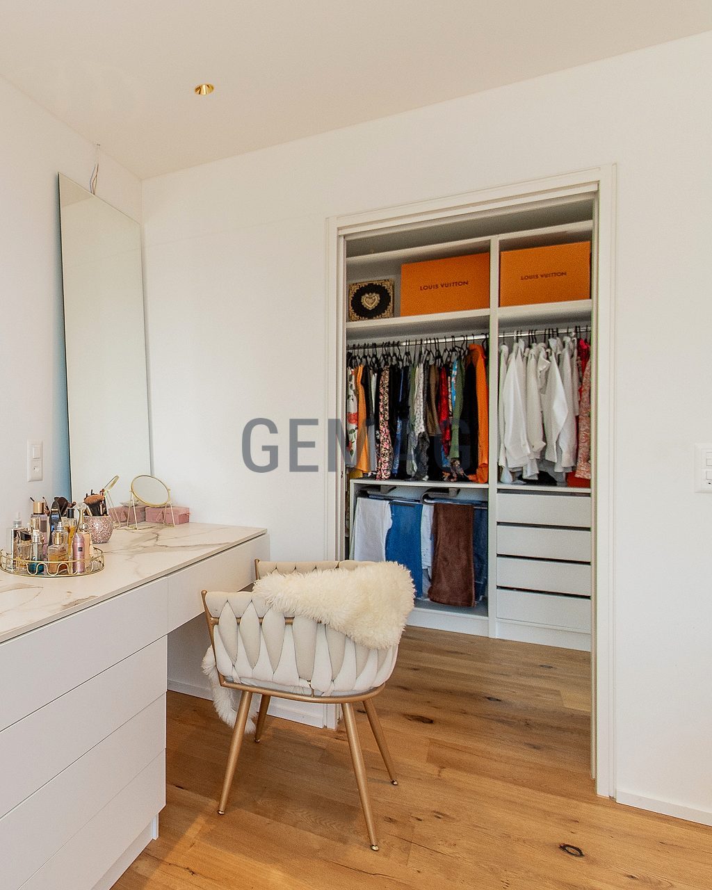 Schminktisch mit Marmorplatte und Spiegel, dahinter offener Kleiderschrank mit Kleiderstange, Holzboden.