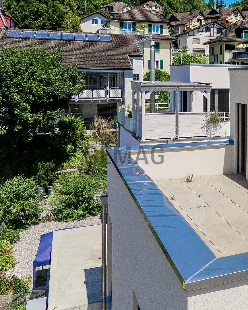 Draufsicht auf eine flache Dachterrasse mit Terrassenplatten, Schiebetür und Pergola im Hintergrund.