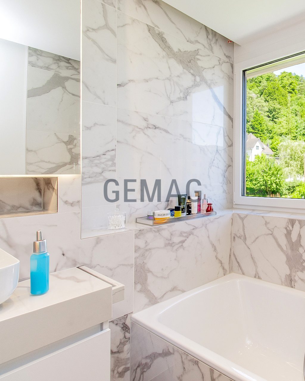 Badezimmer mit marmorierter Wandverkleidung, Einbauwanne und Fenster mit Grünblick.