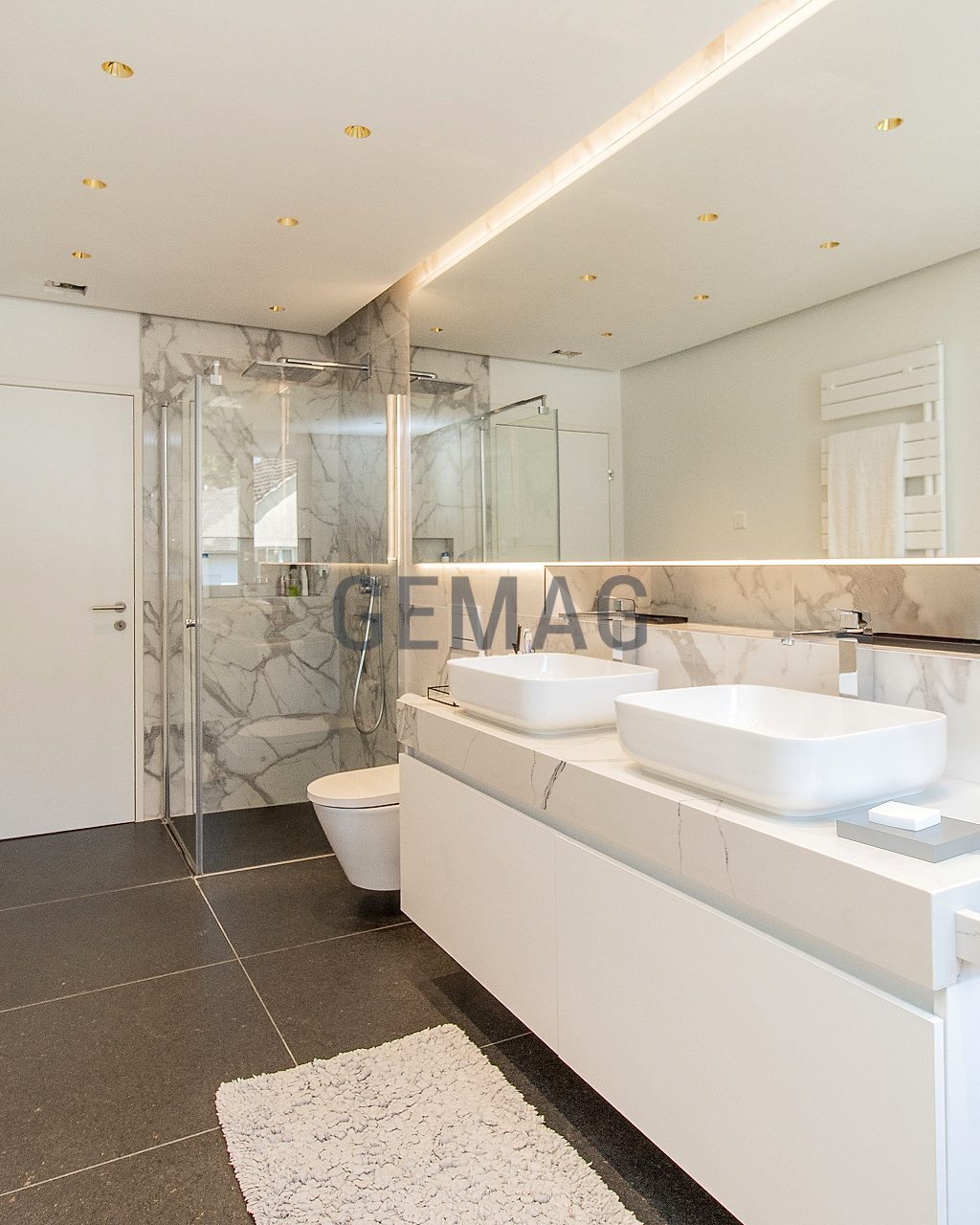 Badezimmer mit Doppelwaschtisch, Glasdusche und Marmorverkleidung, Blick von der Seite.