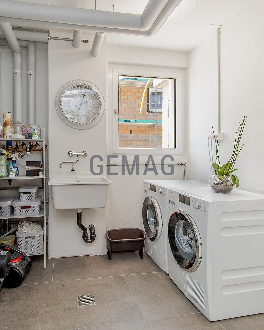 Hauswirtschaftsraum mit Waschmaschine, Tumbler, Waschbecken und Wasserboiler, Frontalperspektive.