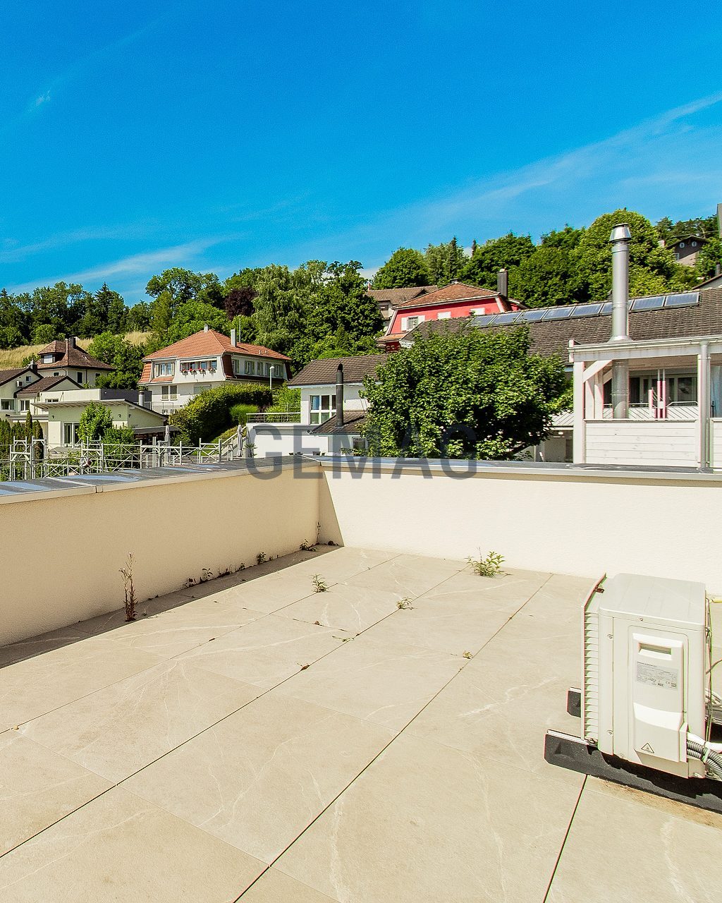 Geräumige Dachterrasse mit hellem Plattenbelag und Blick auf umliegende Wohnhäuser und begrünten Hang.