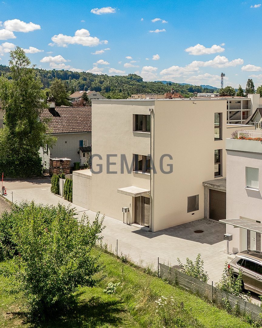 Drohnenaufnahme eines modernen, hellverputzten Einfamilienhauses mit Flachdach, Carport und umliegender Wohnbebauung.