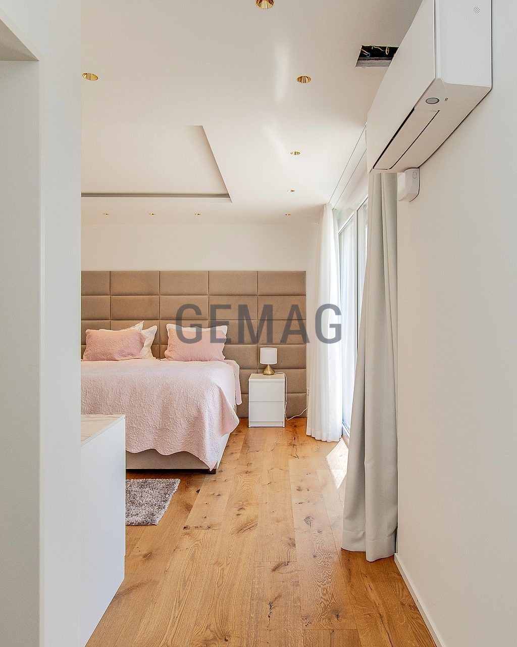 Blick durch den Eingangsbereich in ein Schlafzimmer mit Doppelbett, gepolstertem Kopfteil und Holzboden.