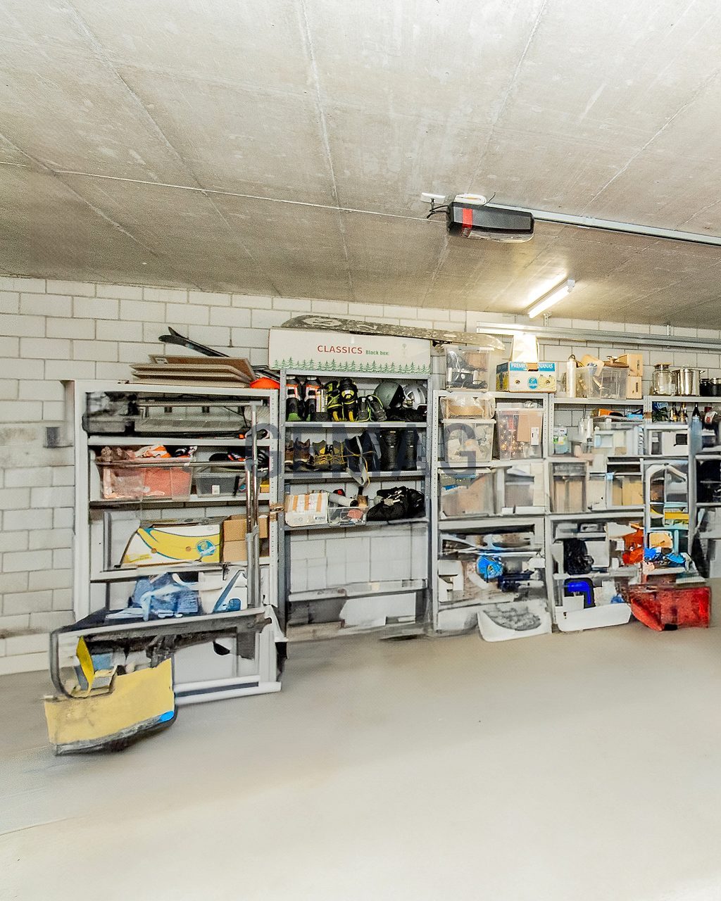 Innenansicht einer Einzel­garage mit Sektionaltor, Betondecke und gefüllten Metallregalen an der Rückwand.