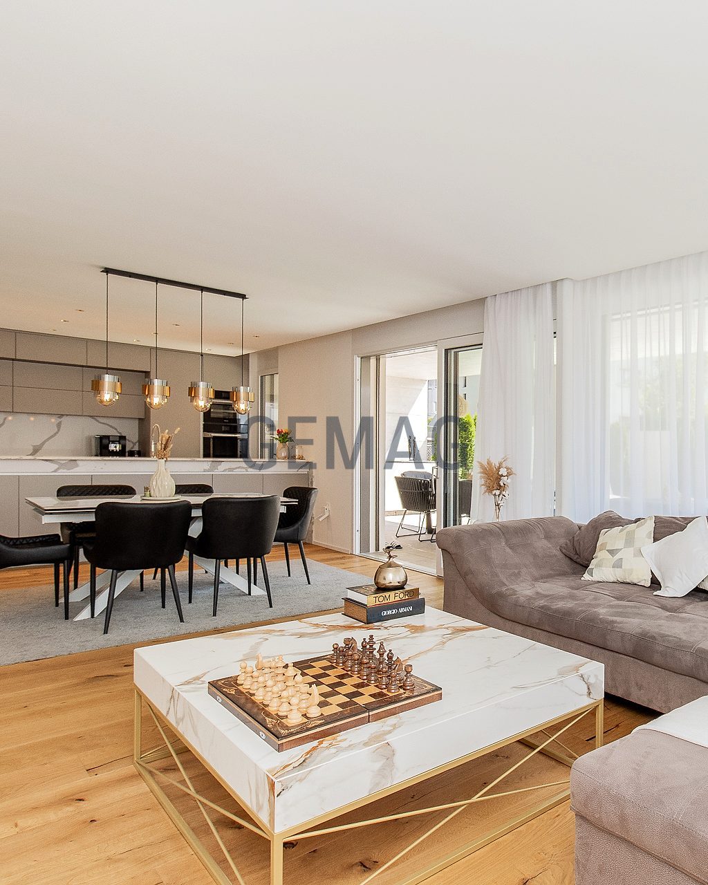 Wohnzimmer mit Sofa und Couchtisch, dahinter Esstisch mit Stühlen und offene Küche, Zugang zur Terrasse.