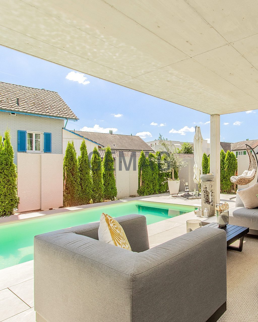 Überdachte Terrasse mit Lounge-Möbeln und Swimmingpool im Garten, Blick in den Aussenbereich.