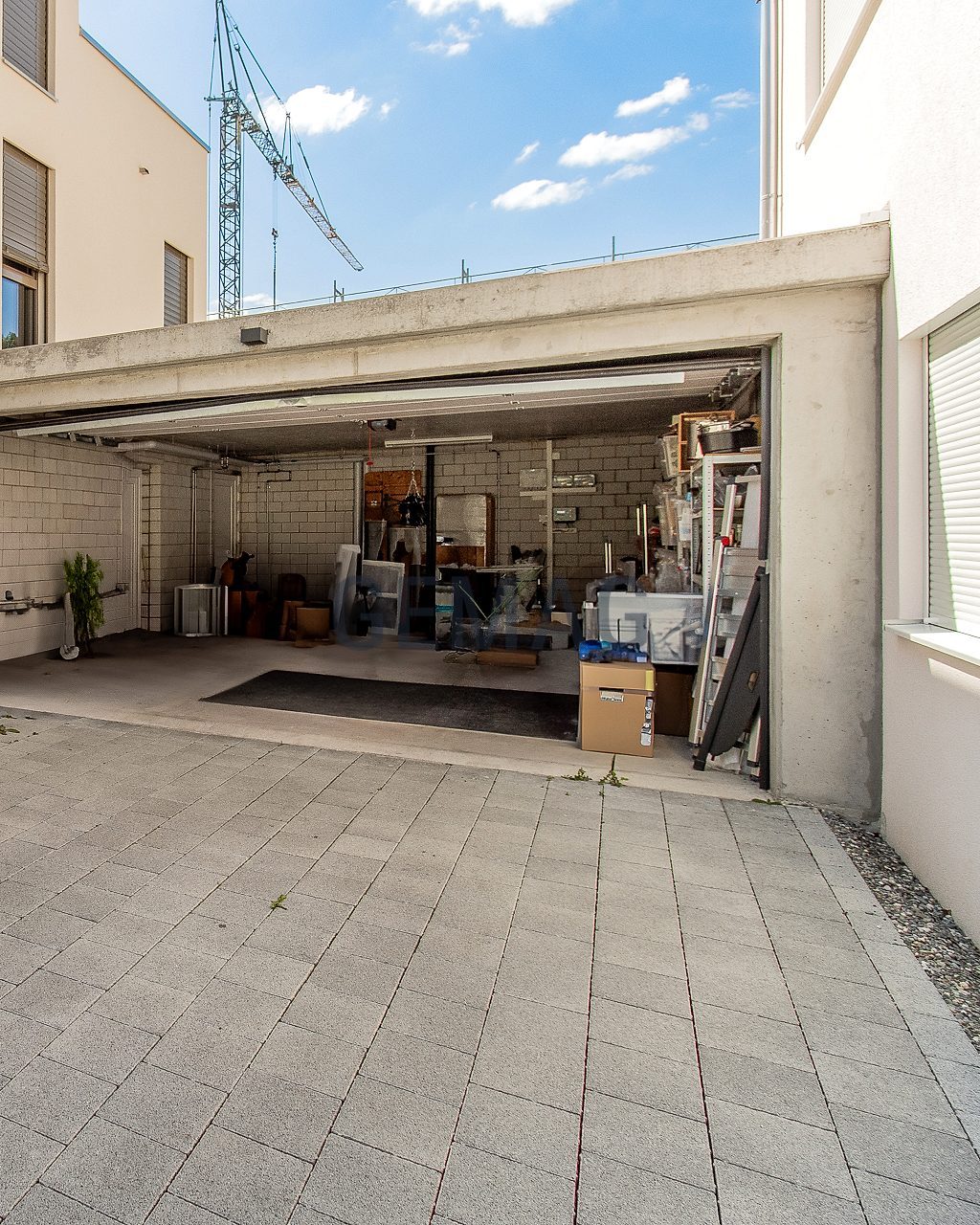 Gepflasterter Vorplatz mit offener Garage im Erdgeschoss, Blick von aussen in den Lagerbereich.