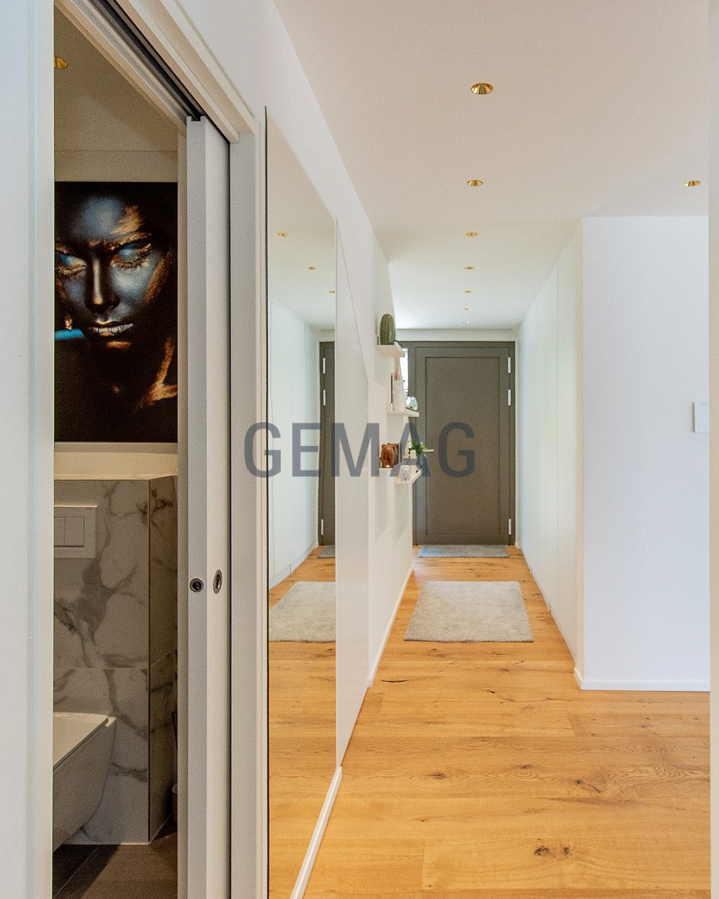 Flur mit Holzboden, offener Garderobe rechts und Blick zur Eingangstür, links geöffnete Schiebetür zum WC.